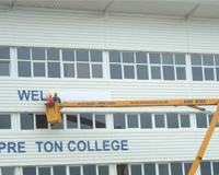 Two workers in the basket of Cherry Picker applying a sign to the front of Preston College